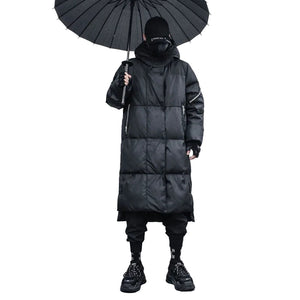 Person wearing a long black puffer coat holding a black umbrella against a textured wall.