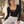 Model sitting on a cafe bench in the black bodysuit and light heather sweatpants, coffee cup in hand