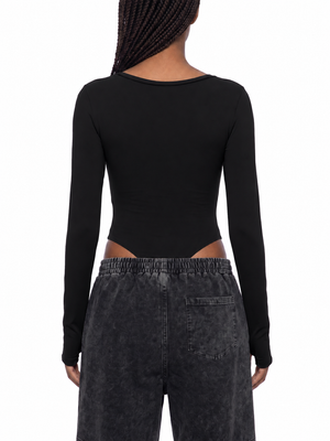 Back view of the black bodysuit on a model, plain back, high-cut legs and thumbholes at the cuffs