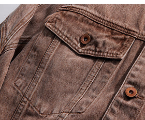 Nærbillede af klaplommen på brystet med en kobberfarvet knap på den falmede brune denim