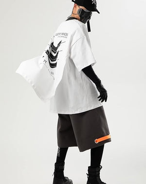 Person wearing a white oversized shirt with black text and graphics, black shorts with an orange stripe, and black shoes on a light gray background.