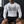 A tattooed man sits on a locker room bench in the white compression shirt, front view with shorts