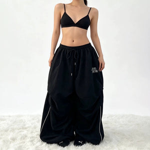 Black parachute y2k pants in front view with the drawstring tied at the waist and white piping on the side seams