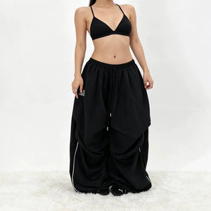 Μαύρο παντελόνι parachute με φαρδύ μπατζάκι σε γυναίκα με bralette, μπροστινή όψη των oversized σουρωμένων μπατζακιών και του passepoil