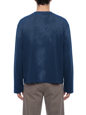 A model wears the navy long sleeve tee from behind, hem sitting square at the hip over trousers