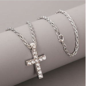 Zilverkleurige iced kruishanger aan een gedraaide koordketting met karabijnhaak, rustend op een grijze cilinder