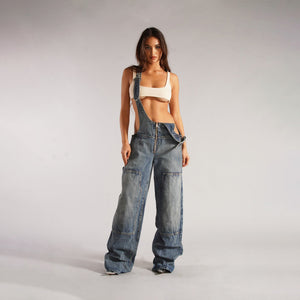 Zip Denim Y2K Overalls in mid blue, front view with patch pockets and one strap worn loose
