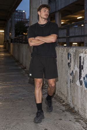 Model with arms crossed in the Black zip pocket basketball shorts and a black tee, front view in a garage
