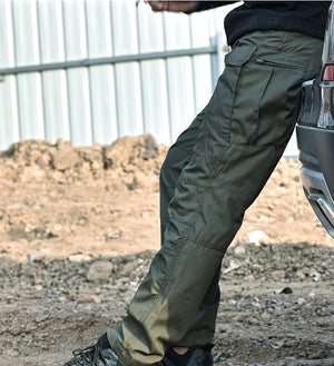 Green cyberpunk pants on a man leaning on a car, side view of the zipped thigh pocket and knee panel seams