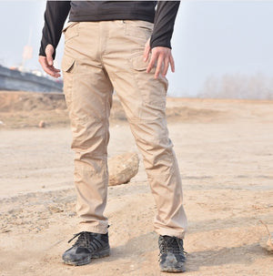 Khaki tactical cargo pants worn by a man standing on sandy ground, front view with flap pockets on both thighs
